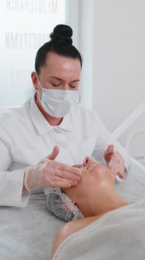 Kozmetik uzmanı özel nemlendirici krem uyguluyor, güzel beyaz bir kadının yüzünü ovuyor, soyuyordu. Güzellik salonunda yüz bakımı yaşlanmayı önleyen kozmetik masaj prosedürü. Güzellik tedavisi