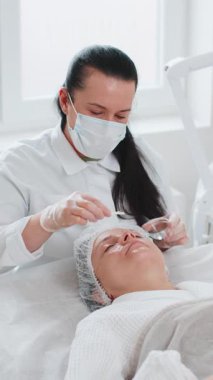 Kozmetik uzmanı özel asit serumu uyguluyor. Tıbbi kremi nemlendiriyor, güzel beyaz bir kadının yüzünü ovuyor. Güzellik salonunda yüz bakımı yaşlanmayı önleyen kozmetik tedavi prosedürü