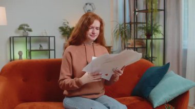 İş çizelgelerini ve grafikleri inceleyen ve ödenmemiş faturaları evdeki oturma odasındaki kanepede oturarak havaya atan, stresli, Kafkasyalı genç kadın. Kızgın kızıl saçlı uzaktan kumandalı kız koltukta çalışıyor..