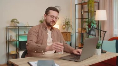 Ofis odasında dizüstü bilgisayarla çalışırken masa başında oturmuş su içen Kafkasyalı bir iş adamı. Genç erkek serbest çalışan adam bilgisayar ekranı internette geziniyor..