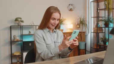 Olgun bir iş kadını akıllı telefon daktilo kullanarak evet diyor, başarıyı kutluyor piyango hedefini başarıyla kazanıyor olumlu haberler, zafer. Evde oturan kız.