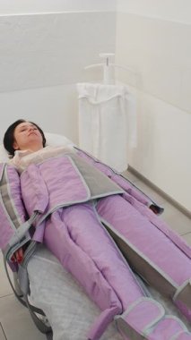 Basınç tedavisi gören kadın hasta, tıp yatağında uzanıyor ve dinleniyor. Şişkinlik ve selülite karşı kullanılan donanım kozmetolojisi tekniği. Giyside bulunan sıkıştırılmış hava ile lenfatik sistemi etkiler.