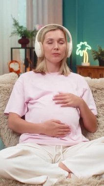 Evde orta yaşlı hamile bir kadın meditasyon kulaklıklarıyla sürekli nefes alıp veren okyanus dalgaları çalıyor. Kanepede dinlenen beyaz kız ellerini karnına koyuyor. Huzuru hissediyor. İç huzuru sağlıyor..