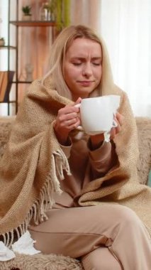 Genç, hasta, yetişkin bir kadın battaniyenin altında kanepeye oturur, bir fincan sıcak çay ve sıcak ellerle nazikçe burnunu çeker. Sarışın kız yorgun ve hasta görünüyor. Soğuk belirtilere sakin bir ifadeyle tepki veriyor..