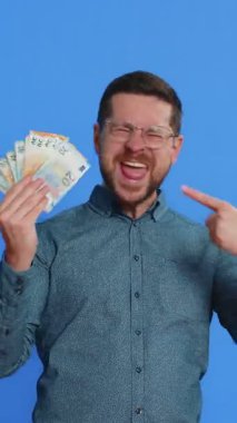 Zengin, mutlu, orta yaşlı, gözlüklü, mutlu bir beyaz adam elinde para, euro nakit para, hayran gibi banknotlar, başarılı iş kariyeri, piyango talihlisi, büyük gelir kaynağı. Mavi arkaplanda izole edilmiş adam