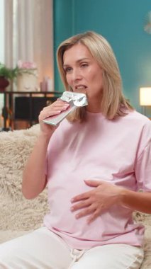 Hamile, orta yaşlı bir kadın, zevkle yuvarlanan gözlerle çikolata tadıyor karnına sürtünüyor ve tadını çıkarıyor. Kanepede oturan beyaz bir kız hamilelik sırasında zevk almanın tadını çıkarıyor..