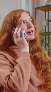 Gülümseyen beyaz kız evdeki kanepede oturan arkadaşlarıyla telefon görüşmesi yapıyor. Gündelik giysiler içinde mutlu bir kadın modern bir evde dedikodu yapmaktan zevk alıyor..