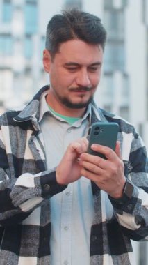 Kafkasyalı yetişkin erkek turist dışarıda cep telefonuyla internette sohbet ediyor. Mutlu, orta yaşlı bir adam cep telefonu kullanıyor. Şehir merkezindeki bir caddede SMS ile iletişim kuruyor..