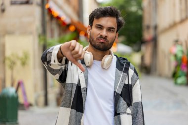 Hoşlanmamak. Üzgün Arap genç adam işaret dilini gösteriyor, hoşnutsuzluğunu dile getiriyor, tatminsiz kötü işler yapıyor, açık havada hata yapıyor. Şehir sokağındaki hoşnutsuz İspanyol adam..