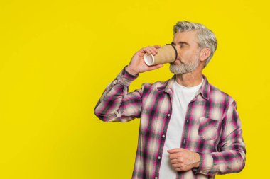 Olgun bir adam hafif kağıt bardak tutar, sakin bir ifadeyle kahve aroması kokar. Orta yaşlı bir adam sarı arka planda sabah kahvesini içiyor, erken rutin zevkleri yansıtıyor.