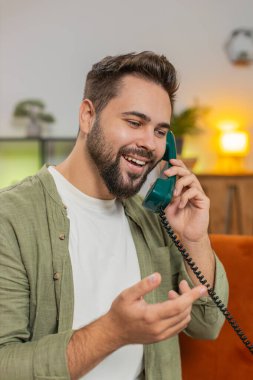 Gülümseyen genç adam evdeki kanepede oturan arkadaşlarıyla telgraflı telefon görüşmesi yapıyor. Mutlu, heyecanlı esmer erkek. 90 'ların modası geçmiş eski moda telefonlardan hoşlanıyor. Oturma odasında konuşuyor..