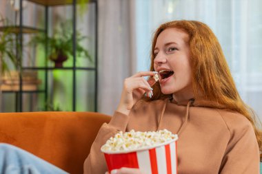 Rahatlamış kızıl saçlı genç bir kadın patlamış mısır yiyor ve evdeki oturma odasında kanepede oturup film seyrediyor. Mutlu kızıl elbiseli kız hafta sonu boyunca dairede film izlemekten zevk alıyor..