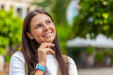 Düşünceli gülümseyen mutlu esmer kadın, dalgın bir ifadeyle, bir çözüm düşünüyor, şüpheli bir soru soruyor, dışarıda hayaller kuruyor. Şehir caddesinde duran yetişkin kız..