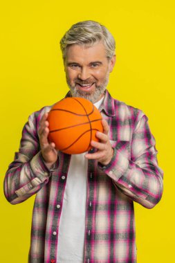 Olgun bir erkek, basketbolu ustalıkla elinde zıplatır, oyun oynar, kendine güvenini gösterir, kontrollü davranır. Sarı arka plandaki orta yaşlı adam atletik inceliği, parmak ucunda dönen topu gösteriyor.