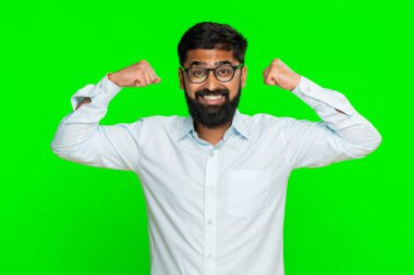 Hintli adam kollarını esnetiyor kendine güvenen bir gülümsemeyle fiziksel gücü, gururu ve motivasyonu ifade ediyor. Yeşil krom anahtar arka planda izole edilmiş Arap adam güç ve kendine güven enerjisini gösteriyor.