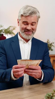 Merkez ofisteki orta yaşlı işadamı, yeni maaş gelirlerini de hesaba katarak avro banknotları sallıyor. Masadaki serbest çalışan adam büyük bir zaferin tadını çıkaran ikramiye planlama yatırımları yapıyor..