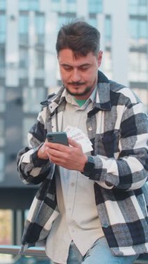 Akıllı telefon kullanan ve para sayan mutlu zengin iş adamı turist Ukrayna Hrivnias UAH nakit banknotları şehir merkezinde duruyor. Başarılı iş kariyeri, piyango kazananı, büyük gelir, zenginlik.