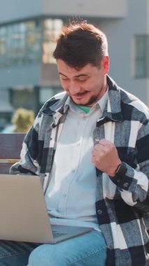 Mutlu, mutlu, olgun bir adam dizüstü bilgisayarda çalışırken zafer çığlıkları atıyor. Başarılı bir jest, dışarıda kazanılan oyunu kutluyor. Şehir merkezinde oturan mutlu yetişkin erkek turist..