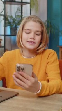 Beyaz çocuk evde dizüstü bilgisayarla sanal okul yarışmasını kazanıyor. Pozitif sınav sonuçlarına ulaşmak, sevinçle atlamak ve akıllı telefonu masaya oturtup mutluluğu ifade etmek.