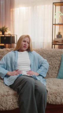 Genç hasta kadın karnını tutuyor ve sindirim bozukluğundan kaynaklanan krampları ve ekşimeleri ortaya çıkarıyor. Kanepedeki beyaz kız koruyucu pozisyonda yatıyor, acı dolu gerilime katlanıyor ve huzur arıyor..