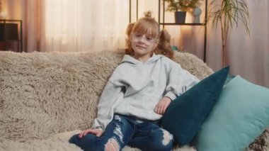 Evde mutlu bir ifadeyle baş parmak gösteren genç kız, mutluluk ve memnuniyeti yansıtıyor. Beyaz çocuk başarının tadını çıkarıyor ve koltukta otururken onayını veriyor..