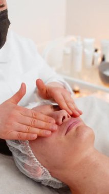 Deneyimli terapist kadın rahatlatıcı spa yüz masajını elleriyle yapıyor. Kuaförde pürüzsüz ve sağlıklı cilt bakımı. Detoks, iyileşme. Yüz fiziksel kozmetoloji oturumunda bir müşteri