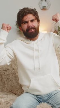 Mutlu Hintli genç adam TV izlerken bağırıyor, başarıyı kutluyor, kazanıyor, gol başarısı iyi haber, piyango şansı, oturma odasında koltukta oturan zafer. Yetişkin adam sınıfta yumruklarını sıkıyor..