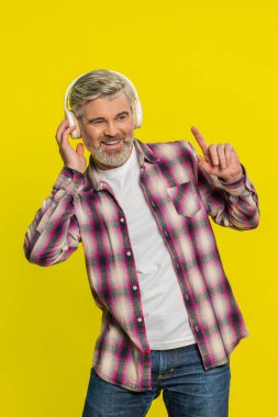 Kulaklıkla müzik dinleyen, dans eden, eğlenen, el kol hareketi yapan orta yaşlı mutlu bir adam. Yetişkin bir adam sarı arka planda kapalı yerde izole edilmiş.