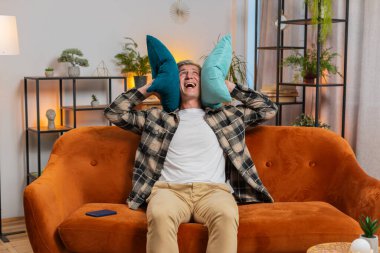 Komşularda tamirat. Sinirli beyaz adam, gürültülü müzik komşularının baş ağrısı sessizliğinden rahatsız olduğu yastıklarla kulaklarını kapatıyor. Evde ses yalıtımı olmayan ince duvarlar.