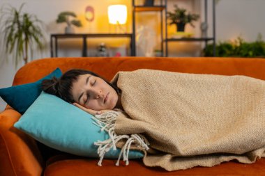 Kanepede battaniyeyle uyuyan yorgun beyaz kadın. Mutlu kız kanepede uzanıp rahatça uyuyarak oturma odasında huzur içinde dinleniyor. Sağlıklı uyku konsepti.