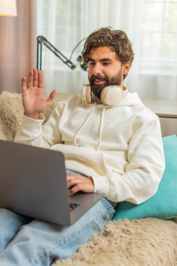 Mutlu genç İspanyol serbest çalışan web kamerasına konuşan meslektaşları ya da uzaktan arkadaşlarıyla çevrimiçi video konferans görüşmesi yapıyor. Hintli yetişkin adam evdeki oturma odasındaki kanepede dizüstü bilgisayar kullanıyor..