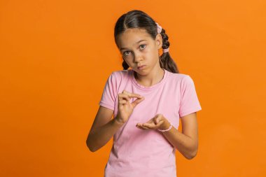 Biraz daha, lütfen bana ver. Genç bir kız çocuğu, küçük bir jest yapıyor, kuşkucu bir gülümseme takınıyor, minimum boyut gösteriyor, yalvarıyor. Turuncu arka plandaki çocuklar