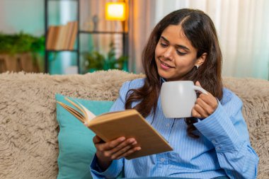 Hindistanlı genç bir kadın, sabah kahvesini evde kitap okurken, sakin ve düşünceli hissediyor. Arap kızı sıcak bir içkiyle huzurlu bir anı kucaklıyor ve sabahın erken saatlerinde edebi odaklanıyor..