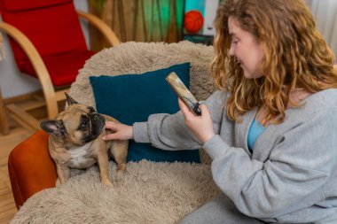 Beyaz saçlı genç bir kadın akıllı telefonuyla evde kanepede oturan köpeğinin fotoğrafını çekerken gülümsüyor. Kız tatlı bir anı yakalar ve tüylü arkadaşı ve kamerasıyla eğlenceli bir bağ kurar..