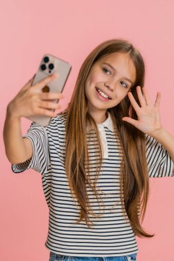 Genç kız, akıllı telefondan yakın bir arkadaşından, mutlu bir şekilde el sallayan, gülümseyen ve heyecanlı bir şekilde konuşan mutlu ve anlamlı bir video mesajı alır. Pembe arka plandaki okul çocuğu.