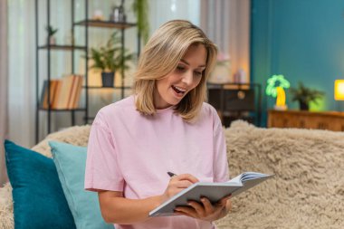 Hamile orta yaşlı bir kadın parmak kaldırma fikrinden mutlu bir şekilde not defterine bebek ismi yazıyor. Kanepede oturan beyaz bir kız, mutlu bir şekilde gülen bebeğin gelecekteki adını belirtir..