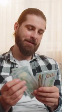 Genç adam evdeki yeni kazanç maaşını kontrol ediyor, her para dolar banknotunu yavaş yavaş mutlu bir ifadeyle sayıyor. Kafkasyalı gülümseyen adam ortak finansal hedefler için fon sağlandığı için mutlu.