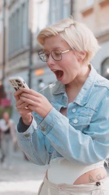 Kafkasyalı genç bir kadın cep telefonuyla kutlama yapıyor iyi haber kazanıyor, piyango büyük ikramiyesi kazanıyor, açık havada dağıtıyor. Şehir caddesinde zıplayan mutlu sarışın bayan turist. Kasaba yaşam tarzları.