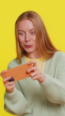 Mutlu, orta yaşlı, heyecanlı beyaz kadın akıllı telefonda yarış arabası simülatörü oyunu oynuyor. Yetişkin kız oyuncu sarı arka planda büyük ikramiyeyi kazandı.