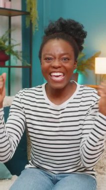 Afrikalı Amerikalı kadın zafer haberlerini kutluyor. Kanepede yükselmiş ellerle zıplamak, neşeli enerji, mutlu duygu kapalı alanda başarılı bir an. Ev ortamında heyecan ve olumlu tepkiler