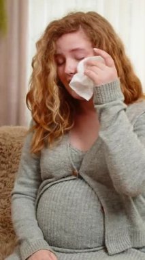 Hamile genç bir kadın kanepesinde oturmuş karnını nazikçe tutuyor gözyaşlarını duygusal bir ifadeyle siliyor, hassas ve düşünceli hissediyor. Kız anneliğin zorluklarını ve derin duygularını benimsiyor..