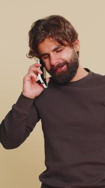 İlgisiz genç Hintli adam, akıllı telefonda can sıkıcı konuşmalar yapıyor. Uykulu yetişkin adam arkadaşıyla cep telefonuyla konuşuyor, çevrimiçi konuşmaları stüdyo bej arka planında izole ediyor..