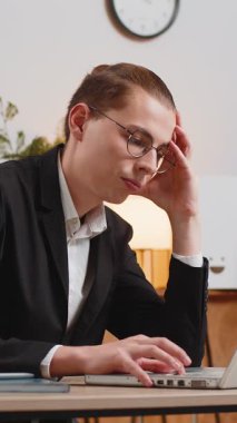 Sıkıcı, genç, uykulu, Kafkasyalı iş adamı dizüstü bilgisayar esnemeleri üzerinde çalışıyor, ofis masasında el ele tutuşuyor. Yorgun ve serbest çalışan işkolik bir adam. İstihdam, işsizlik, meslek.