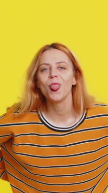 Bluzlu, beyaz tenli sarışın kadın kameraya surat yapıyor, dalga geçiyor, şakalaşıyor, alay ediyor, alay ediyor, dalga geçiyor, taciz ediyor. Sarı arka planda izole edilmiş genç bir kız.