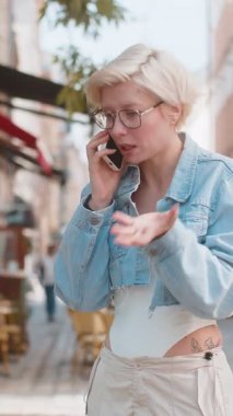 Kızgın kızgın kızgın, Avrupalı genç bir kadın telefonda tartışırken sinirli bir şekilde dışarıda bağırıyor. Şehir caddesinde sarı saçlı, hoşnutsuz, kızgın bir kızı gücendirdim. Kasaba yaşam tarzları.