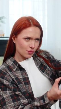 Evde oyun oynayan genç bir kadın konsol kumandası kullanıyor ve yoğun oyunlara duygusal tepki veriyor. Kanepede oturan beyaz saçlı kız enerji, eğlence ve heyecanla oyun seansının keyfini çıkarıyor.