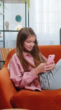 Akıllı telefon sosyal medya uygulamaları üzerinden rahatlama filmi izlerken mesajlarını paylaşan genç bir kız. Beyaz kız çocuk cep telefonu kullanıyor. Oturma odasındaki koltukta oturuyor.