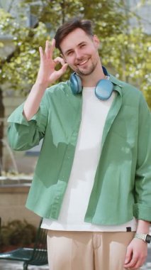 - Tamam. Mutlu, genç, beyaz bir adam kameraya bakıp onaylıyor. İyi bir jest yapıyor. İşaret gibi olumlu bir şey. Şehir caddesinde, açık havada neşeli bir adam.