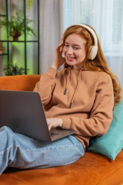 Kablosuz kulaklıklı mutlu, gevşemiş Kafkas genç kadın evinde oturuyor ve dizüstü bilgisayar ağı üzerinde çalışırken disko müziği dinliyor. Kızıl saçlı kız hafta sonu aktiviteleri.