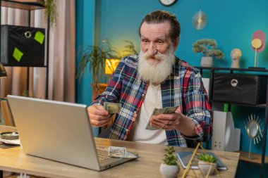 Kafkasyalı kıdemli adam nakit para sayıyor ve ofisteki bilgisayarı kullanıyor. Başarılı serbest çalışan büyükbaba makama yığınla para getiriyor kar paylarını hesaplıyor maaş gelirlerini finanse ediyor